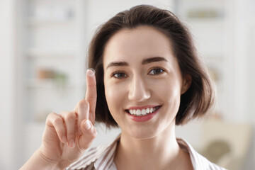 Happy woman with contact lens on her finger indoors