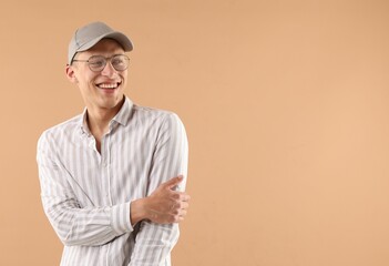 Young man in stylish baseball hat on beige background, space for text