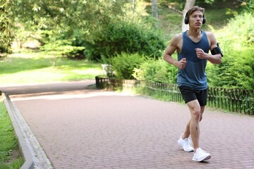 Sporty man with headphones running in park, space for text