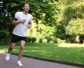 Sporty man with armband running in park, space for text
