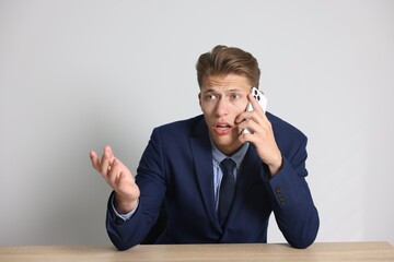 Young businessman complaining to someone via phone at wooden table indoors
