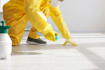 Pest control worker in protective suit spraying insecticide indoors, closeup