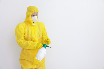 Pest control worker in protective suit spraying insecticide near white wall. Space for text