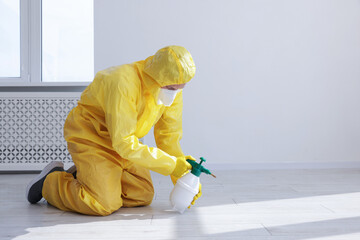 Pest control worker in protective suit spraying insecticide indoors. Space for text