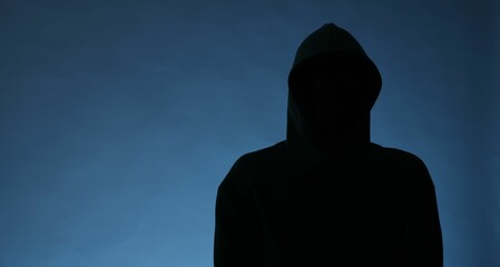 Silhouette of anonymous man in hood on blue background, space for text
