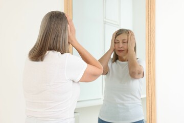 Beautiful senior woman near mirror indoors, selective focus