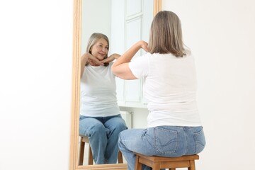 Beautiful senior woman looking at herself in mirror indoors