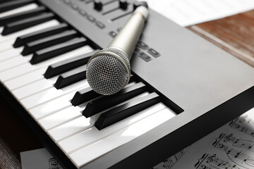 MIDI keyboard, microphone and music sheets on table, closeup
