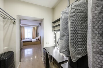 cozy room scene with a bedroom view through a doorway, alongside a vanity with a mirror, garment...