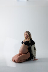 Beautiful pregnant young blonde in leather fashion jacket and panties with open belly stands on...