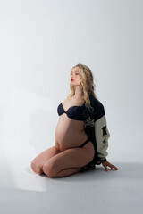 Beautiful pregnant young blonde in leather fashion jacket and panties with open belly stands on...