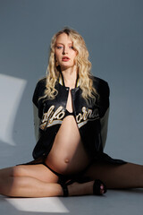 Beautiful pregnant young blonde in leather fashion jacket and panties with open belly stands on...