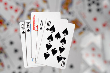 Spread black spades (10, Quinn, King, Ace) with a slightly offset red joker appear to float above a blurred background of scattered playing cards