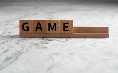 The word "GAME" spelled out using wooden letter blocks resting on a wooden rack, isolated against a light, textured background
