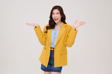 young Asian woman in a yellow blazer and denim shorts smiling brightly while presenting with open...