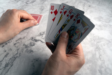 A hand reaches for the final card to complete a royal flush in diamonds (10, King, Queen, Jack of...