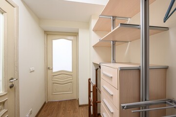 closet featuring wooden shelves, metal supports, drawers, and a door with a glass pane, lit by soft...