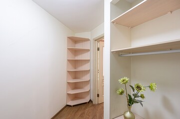 bright room featuring a corner shelf, wooden floors, and a partially visible wardrobe. The space is...