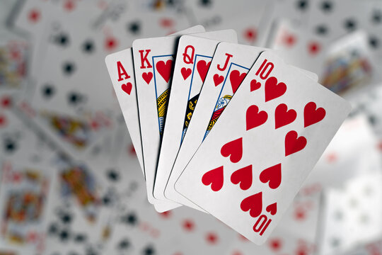 A complete royal flush in hearts fanned out and appearing to float above a blurred backdrop of scattered playing card