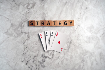 Wooden blocks spelling "STRATEGY" lie above four aces playing cards on a marble background, symbolizing winning tactics and business planning