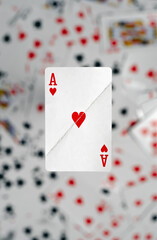 A visibly damaged Ace of Hearts playing card appears to float above a blurred background of deck of cards, conveying wear or a struggle. Broken heart