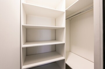 empty white wardrobe with shelves and a hanging rod. The shelves are clean and the space is well-lit