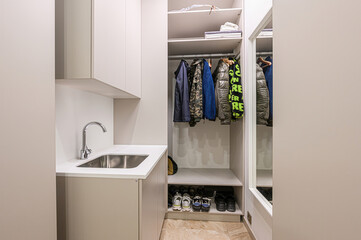 Modern mudroom featuring a sink, cabinets, and a closet with coats and shoes. Neutral tones create...