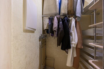 closet interior view with hanging clothes, storage bags, and a modern shelving unit. Neutral wall...