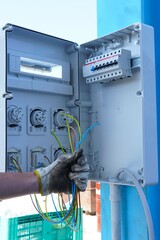 Close up of electrician's hand holding several colored electrical wires while installing a junction box. Electrical work, power supply and professional installation in industrial environment.