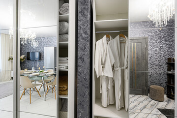 Reflection in wardrobe mirror shows a dining area, while open wardrobe sections display neatly...