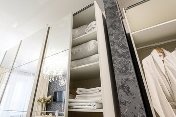 Mirrored closet with shelves and robes. The reflection reveals a room with a chandelier