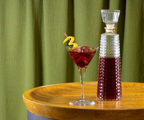 Bottles of cherry liqueur on a wooden table with a green curtain background.