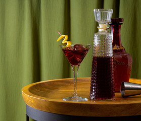 Cocktail and bottles on a wooden table with a green curtain background