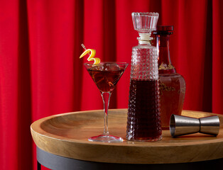 Cocktail and bottles on a wooden table with a red curtain background