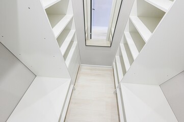 bright, clean walk-in closet featuring white shelving units on either side of a light wood floor,...