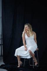 Beautiful pregnant young blonde in a long white silk dress to the floor on a black fabric...