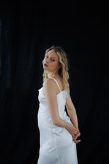 Beautiful pregnant young blonde in a long white silk dress to the floor on a black fabric...