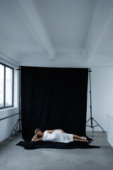 Beautiful pregnant young blonde in a long white silk dress to the floor on a black fabric...