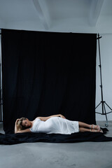 Beautiful pregnant young blonde in a long white silk dress to the floor on a black fabric...