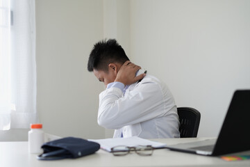 Obraz premium An asian young doctor is getting headache after duty and hand holding and rubbing hurt area, problem in health due to overworked, and holding the medication bottle and taking the pill for pain relief.