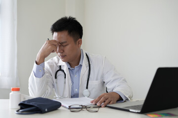 An asian young doctor is getting headache after duty and hand holding and rubbing hurt area,...