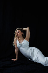 Beautiful pregnant young blonde in a long white silk dress to the floor on a black fabric...