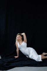 Beautiful pregnant young blonde in a long white silk dress to the floor on a black fabric...