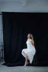 Beautiful pregnant young blonde in a long white silk dress to the floor on a black fabric...