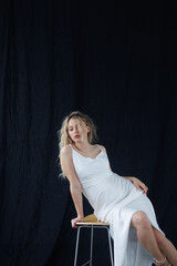 Beautiful pregnant young blonde in a long white silk dress to the floor on a black fabric...