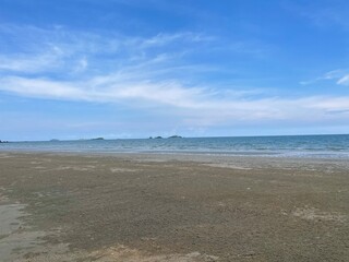 A wide, expansive beach stretches out under a blue sky with wispy clouds, leading to calm ocean...
