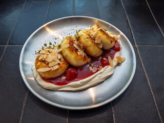 Delicious golden syrniki pancakes garnished with sliced almonds and vibrant red berry sauce for sweet breakfast