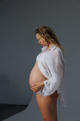 Beautiful pregnant young blonde in white shirt on cyclorama with beautiful lighting. Pregnant girl...