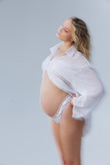 Beautiful pregnant young blonde in white shirt on cyclorama with beautiful lighting. Pregnant girl...