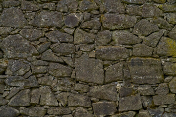 A detailed close up view of a stone wall featuring moss growing on it